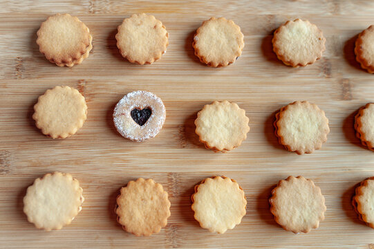 Homemade round shortbread cookies placed in a rows on bamboo plank. One of them is different.