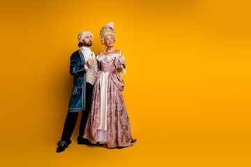 Elegant couple in classic aristocratic costumes on vibrant yellow background reflecting history and...