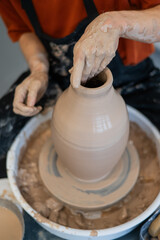 Close-up of a potter's hands making a ceramic vase on a potter's wheel. Vertical photo. 
