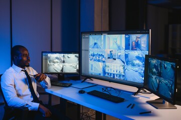 African American security guard looking at desktop computer screen while speaking on walkie talkie