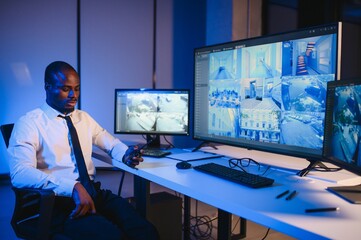 Fototapeta premium African American security guard looking at desktop computer screen while speaking on walkie talkie