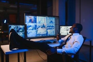 African-American security officer watching the screens talking on radio in control room