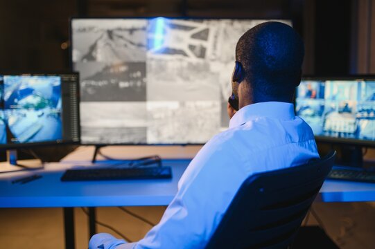 Back view of African American security operator use computer with screens showing surveillance camera footage