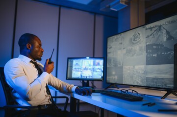 African American security officer or dispatch uses computer and walkie talkie, looks at screens