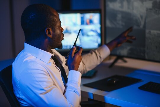 African-American security officer watching the screens talking on radio in control room