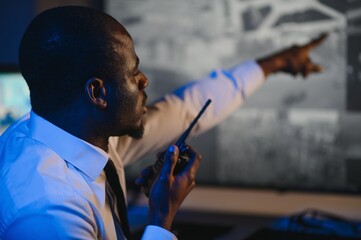 Back view of African American security operator use computer with screens showing surveillance...