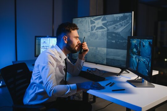 Back view of man watching surveillance footage and map on computers