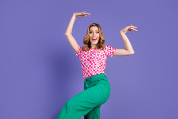 Naklejka premium Cheerful young woman in trendy outfit striking a dynamic pose on a vibrant purple background