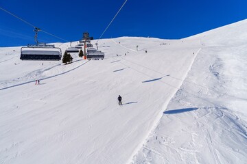 This image shows a skier in a white and black suit going down a snowy mountain slope. In the...