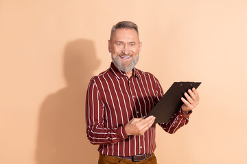 Confident Mature Gentleman Holding a Clipboard on Beige Background Wearing a Stylish Striped Shirt,...
