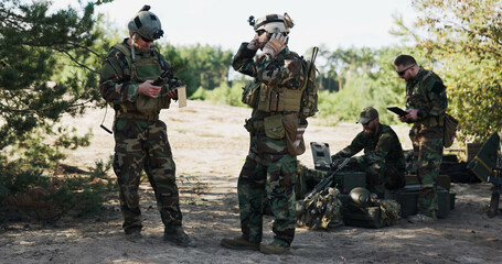 Soldiers plan their field patrol, analyzing strategy and location on a map using a computer and tablet, as the troop leader puts on his helmet before deployment.
