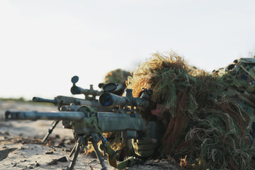 Military men in moro uniforms, dressed in ghillie camouflage with grass and moss, lie concealed on...