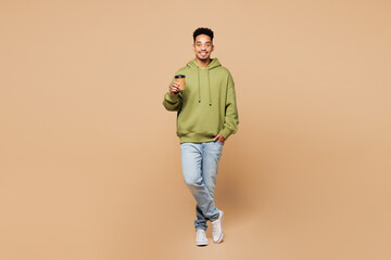 Full body young man of African American ethnicity he wears green hoodie casual clothes hold...