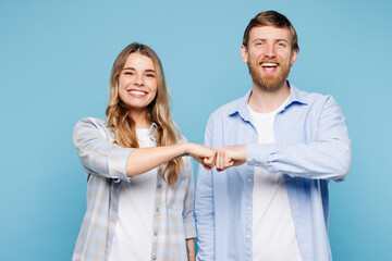 Young smiling couple two friends family man woman wear shirt casual clothes together do fist bump gesture look camera isolated on pastel plain light blue background studio portrait. Lifestyle concept.