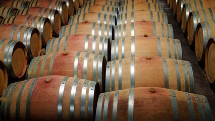 A picturesque view of rows of stacked oak wine barrels in a serene winery cellar, showcasing intricate wood grain details and creating a warm, inviting atmosphere perfect for wine enthusiasts.