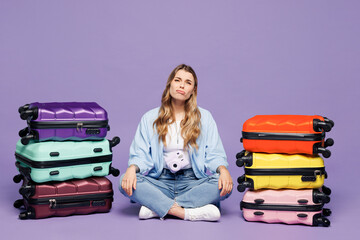 Traveler sad frustrated woman wear blue clothes sit near stack of many bags isolated on plain...