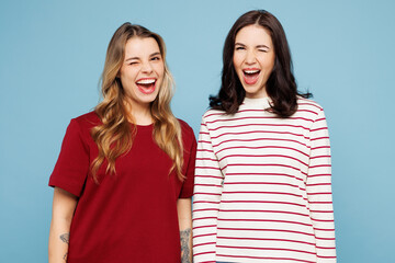 Obraz premium Young cheerful fun cool couple two friends women wearing red casual clothes look camera wink blink eye together isolated on pastel plain light blue cyan background studio portrait. Lifestyle concept.