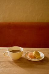 A warm cup of coffee sits beside a plate of colorful macarons on a wooden table in a peaceful cafe setting during the afternoon, creating a perfect moment for relaxation