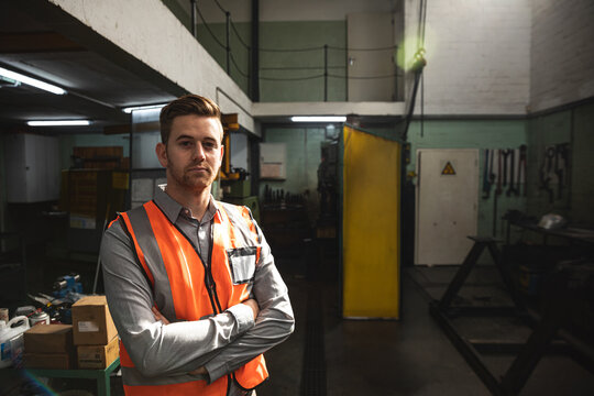 Engineer in orange safety vest standing confidently in hydraulic factory workshop