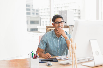 Smiling businessman using computer at office desk, surrounded by creative tools