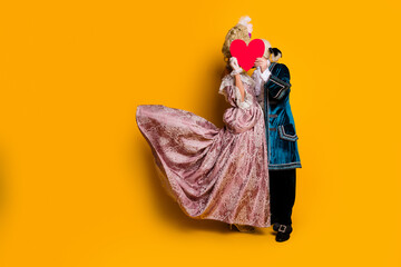 Elegant couple in retro costumes sharing love on vibrant yellow background