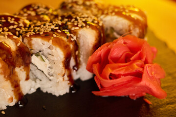 Sushi rolls topped with a glossy sauce and sesame seeds are placed next to vibrant pickled ginger....