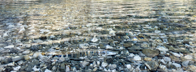 panoramic view of riverbed with stones under clear water. calm surface with gentle ripples and reflections. minimal natural background. neutral