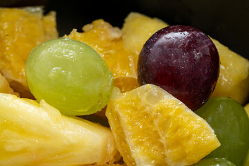 fresh fruit salad, colorful pieces of grape, orange in black background, head on, close up