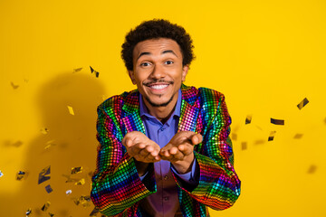 Charismatic young man in a colorful jacket smiling joyfully against a yellow background with...
