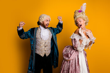 Two friends dressed in vintage royal costume engage actively against a yellow backdrop, showcasing...