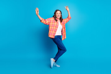 Joyful mature woman dancing on blue background wearing casual vibrant outfit, expressing happiness...