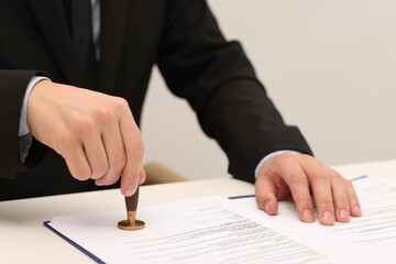 Man stamping licensing agreement document at white table indoors, closeup