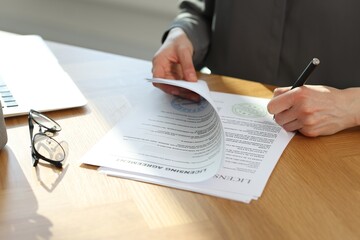 Woman signing licensing agreement document at wooden table indoors, closeup