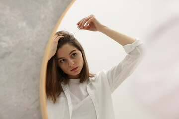 Fototapeta premium Hair loss problem. Girl applying serum onto hairline near mirror in bathroom