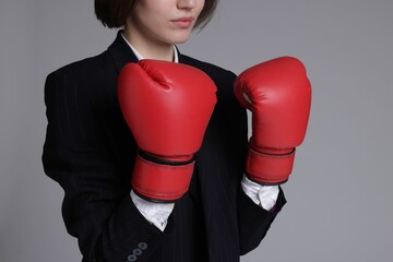 Competition. Businesswoman in suit wearing boxing gloves on grey background, closeup with space for...
