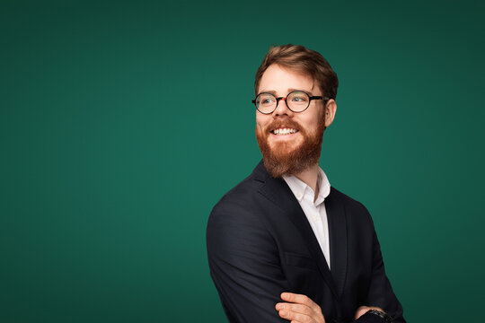 Confident man wearing a stylish suit and glasses against a solid green backdrop, expressing positivity and professionalism.