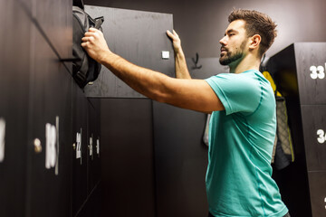 Fit man puts his stuff in the locker of the dressing room in the gym.