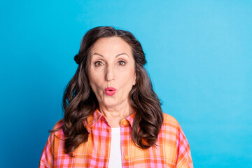 Fototapeta premium Mature woman expressing surprise on a blue background while wearing a colorful checkered shirt
