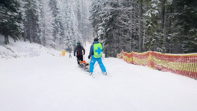 Mountain rescuers transporting an injured skier, going downhill after first aid. Slope rescue, ski patrol service evacuating the victim on a special sledge. Bukovel ski resort, ukraine carpathians.