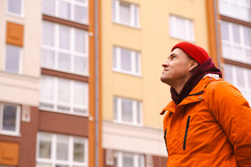 Naklejka premium Young Person in an Orange Jacket With a Red Beanie Gazes Upwards in an Urban Courtyard During Winter