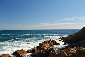 Rocky coastline with ocean waves and sky. Sea waves crashing on coastal rocks. Ocean view with rocky shoreline and water. Coastal landscape with rocks and blue sea. Waves breaking on a rocky beach