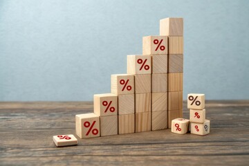 A stack of wooden blocks featuring percentage symbols, arranged in an ascending manner on a rustic wooden surface, symbolizing growth or financial concepts.
