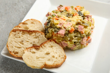 Plate of tasty Olivier salad with bread on light background, closeup