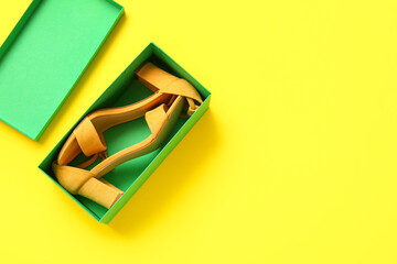 Cardboard box with high heeled sandals on yellow background