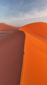 Vertical Aerial view of Dune 45 near Sesriem, Sossusvlei National Park in Namibia, surrounded by giant dunes. People are climbing to the top of the dune at sunset.