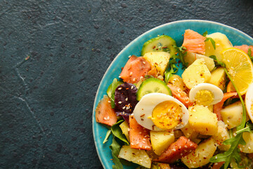Plate of tasty potato salad with eggs and avocado on dark background, top view