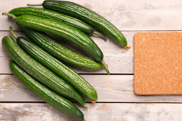 Board with fresh cucumber on light wooden background