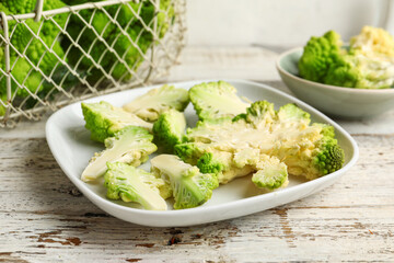 Plate with cut romanesco cabbage on light wooden table