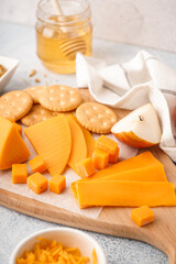Board with tasty cheddar cheese, crackers and pear on light background, closeup