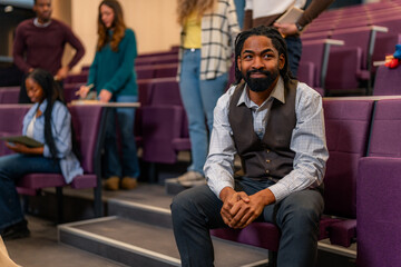 University professor sitting and smiling in lecture hall with students attending lesson